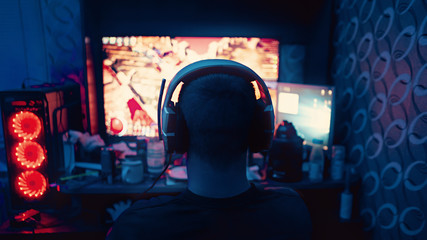 a gamer is sitting in front of a large monitor with headphones, he is an esportsman, a guy of European appearance is shot from the back, a silhouette in headphones against the background of a monitor  © Катя Датунова