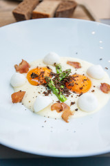 Starter cooked with soft boiled yellow eggs, asparagus, salted meringue and Cretan pork with truffles on top of the dish, served in white plate.