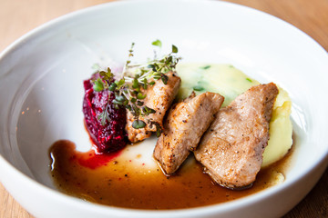 Delicious roasted pork filet cooked with smashed potatoes and smashed beetroots served in white plate.