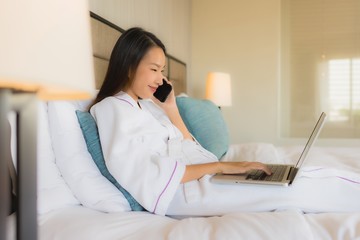 Portrait beautiful young asian women using laptop or computer with mobile smart phone on bed