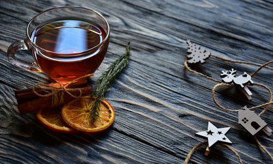 Cup of tea, dried slices of orange and cinnamon sticks with Christmas decorations on a dark wooden background. Festive background.
