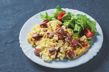 Omelet with sausage and vegetables in white plate on Dark grey black slate background