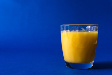  glass of fresh juice and orange on a classic trendy blue background with striped straws