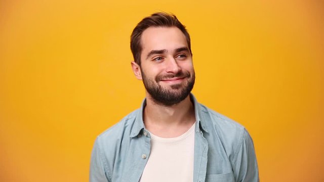 Handsome dreamful bearded young guy 20s in denim shirt white t-shirt isolated over yellow background in studio. People sincere emotions, lifestyle concept. Looking at the camera with charming smile.