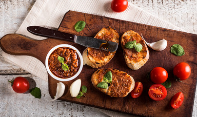Sliced traditional toast bread with tomato pesto and basil on a cutting board and white table