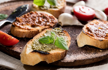 Sliced traditional toast bread with basil and tomato pesto on a cutting board and white table