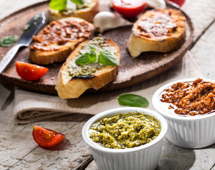 Sliced traditional toast bread with basil and tomato pesto on a cutting board and white table