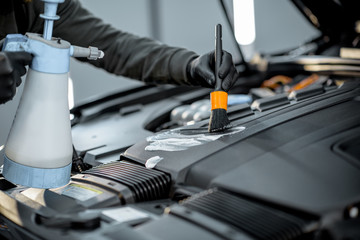Man performs a professional car cleaning, washing engine with brush and detergent at the service station, close-up view