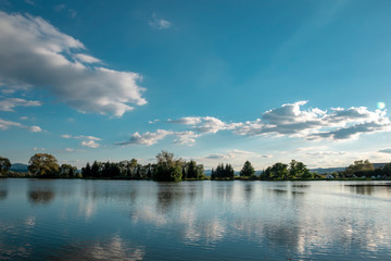 Beautiful fish pond in Badin, near Banska Bystrica, Slovakia. Fishing place. Blue sky and clouds over the lake. Mirror reflection in standing water. Beautiful slovak nature.