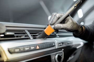 Worker provides a professional vehicle interior cleaning, wiping indoor front panel with a brush at the car service station, close-up