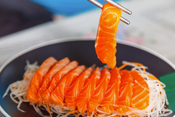  salmon slices are being clamped with chopsticks