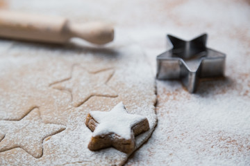 Cookies stars cut out of the dough preparation before baking along with prepared biscuits, rolling pin and cutter.