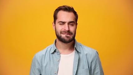 Bearded young guy 20s in denim shirt white t-shirt isolated over yellow background in studio. People sincere emotions, lifestyle concept. Looks at camera, thinks, bites his lip, comes up with ideas.