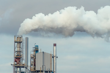 Environmental pollution. Thick gray-white smoke from the industrial pipe of the plant against the blue-gray sky