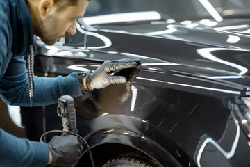 Car service worker examining vehicle body for scratches and damages, taking a car for professional...
