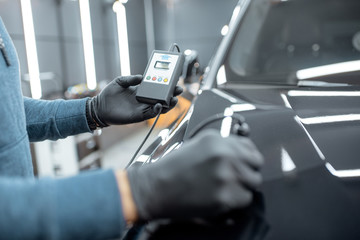 Inspector measuring paint cover thickness of the car body at the vehicle service box, close-up view on hands and professional thickness meter