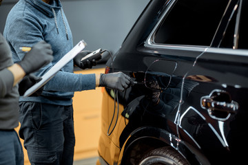 Fototapeta premium Two car service workers examining vehicle body for scratches and damages while taking a car for professional automotive detailing