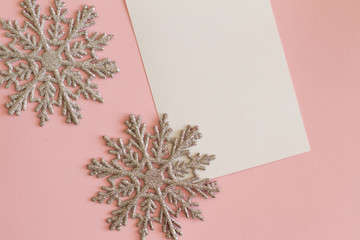 two silver snowflakes on a pink background with a white sheet for writing. . space for text. the concept of new year and Christmas. the view from the top. postcard. banner.