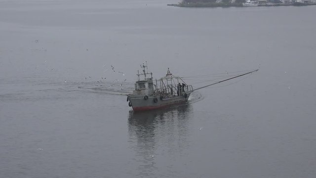 Aerial view of a small fishing ship that catches fish with fishing nets in old trawling