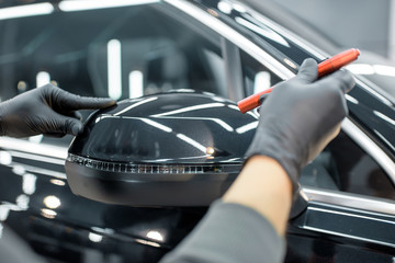 Obraz premium Worker examining vehicle body for scratches and damages backliting by a flashlight at the service. Checking car paint before vehicle detailing