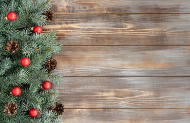 Christmas border with fir branches, red balls and cones on a wooden background.