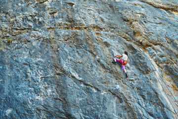 attractive slim young girl climbing on tough sport route on granite cliff, resting and chalking hands. outdoors rock climbing, exercising and active lifestyle concept.