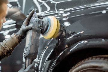 Fototapeta premium Worker polishing vehicle body with special grinder and wax from scratches at the car service station. Professional car detailing and maintenance concept
