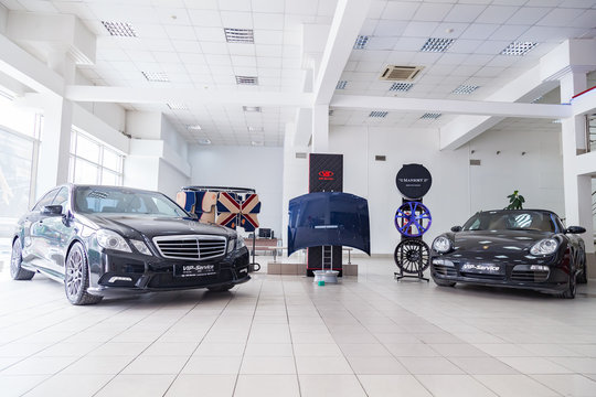 Exhibition at the showroom of a dealership with two black cars Porsche Boxster and Mercedes E during a presentation