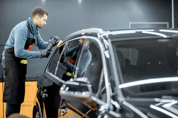 Worker polishing vehicle body with special grinder and wax from scratches at the car service station. Professional car detailing and maintenance concept