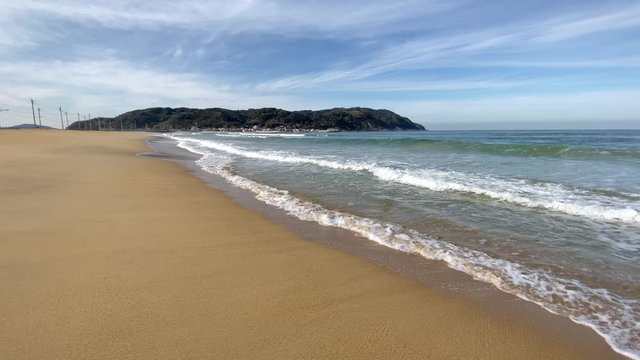 足元に打ち寄せる波を見ながら滑らかな砂浜を歩く トラック 右にパン 全景 志賀島を望む パノラマ 海の中道海岸_v44_00573(ISLL2560_12_MOV)