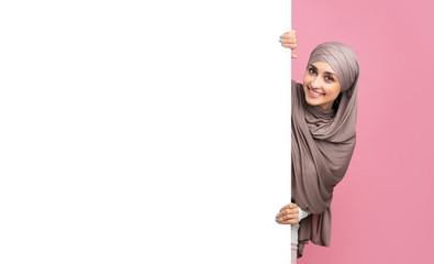 Beautiful arabic woman in hijab standing next to white advertisement board