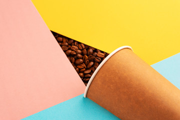 Recycled paper coffee cup on a paper background of colored blocks of yellow, blue, pink colors, creative layout with coffee beans