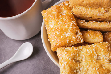Freshly prepared puff pastry with sesame seeds close-up in a white plate and a cup of black tea. Details The concept of home baking, breakfast, snack.