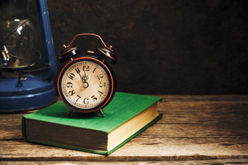 Naklejka premium Old retro alarm clock in rustic interior with books and kerosene lamp.