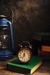 Naklejka premium Old retro alarm clock in rustic interior with books and kerosene lamp.