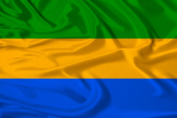 beautiful photo of the national flag of Gabon on delicate shiny silk with soft draperies, the concept of state power, country life, horizontal, close-up, copy space