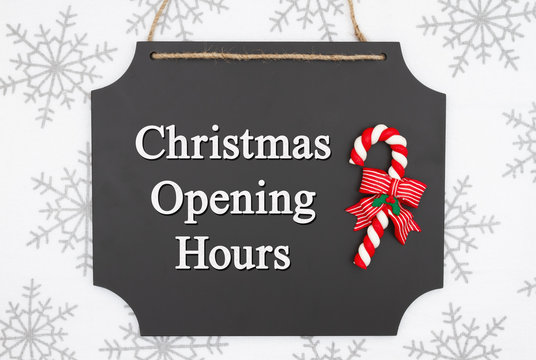 Christmas Opening Hours Message On Hanging Chalkboard With A Candy Cane