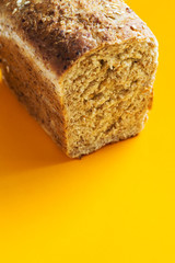 Home baked fresh loaf of bead from spelt whole grain rye flour with seeds bran on bright yellow background. Breakfast healthy diet baking concept