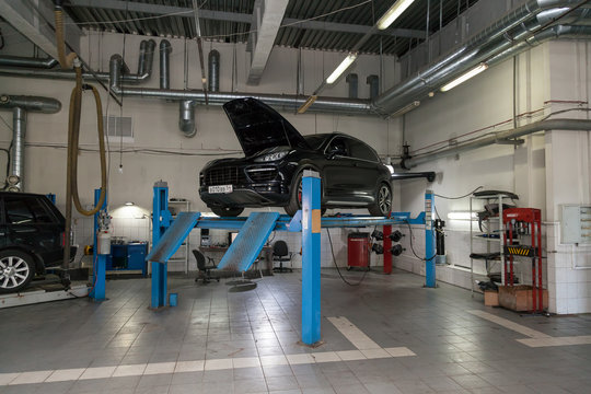 Used Black Car Porsche Cayenne With An Open Hood Raised On A Four-post Lift For Repairing The Chassis And Engine In A Vehicle Repair Shop. Auto Service Industry.