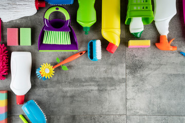 House cleaning concept. Top view of colorful cleaning products on gray tile floor.