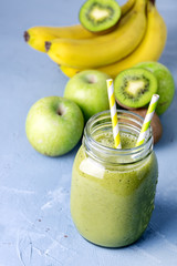Gass Jar of Healthy Detox Green Smoothie on Blue Background Diet Food Fruits Smoothie Raw Bananas Green Apples Kiwi Straws Above Vertical