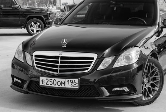 Black Mercedes Benz E-class E250 2010 year front view with dark gray interior in excellent condition in a parking space with gray wall background