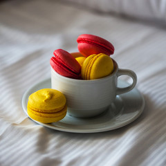 Colorful French macaron pastries in a white circle on the white linen in bed. Red and yellow pasta.