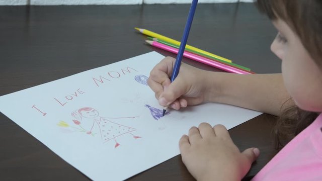 The child draws a mother a gift. Cute little girl draws mom with colored pencils.