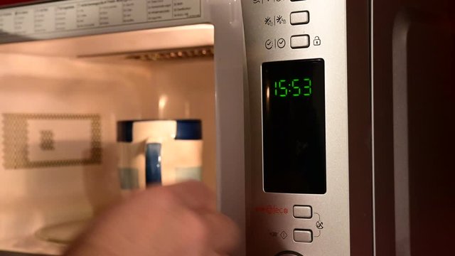 Close-up shot of the microwave oven timer. The oven is opened, the cup is inserted and the timer is set. At the end of the countdown the cup is taken out of the oven.