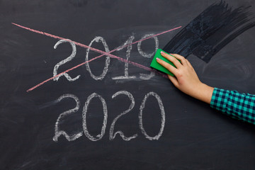 happy new year 2020. Chalkboard with 2020, crossed 2019 and hand with sponge for washing