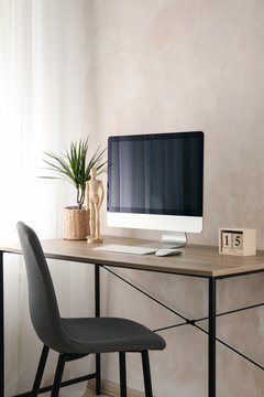 Workplace with computer and plant on wooden table. Light brown background