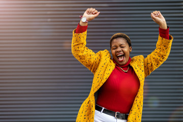 Joyous woman with arms raised in front of a wall 