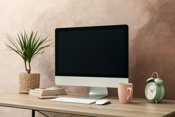 Workplace with computer and plant on wooden table. Light brown background