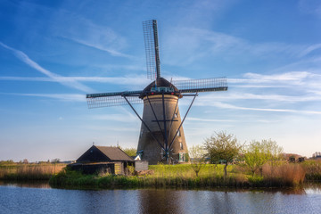 Fototapeta na wymiar Famous Kinderdijk village of mills, popular tourist attraction in Netherlands (Holland), outdoor travel background. Scenic landscape with windmill, water, green grass and blue sky with clouds